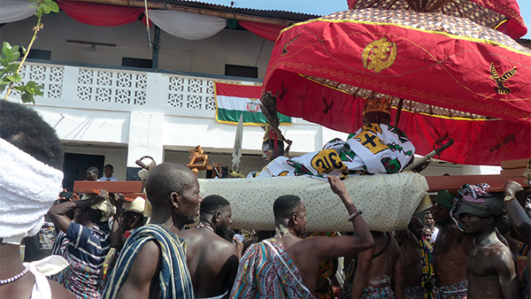 The King of the Ashanti people being carried on a palanquin by his followers. 